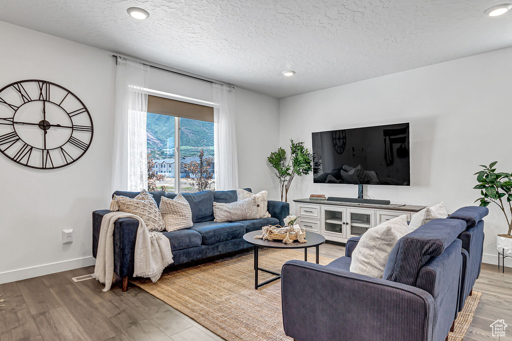 Living room with a textured ceiling, light wood-style floors, recessed lighting, and baseboards