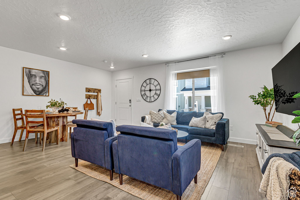 Living area with a textured ceiling, light wood-type flooring, baseboards, and recessed lighting