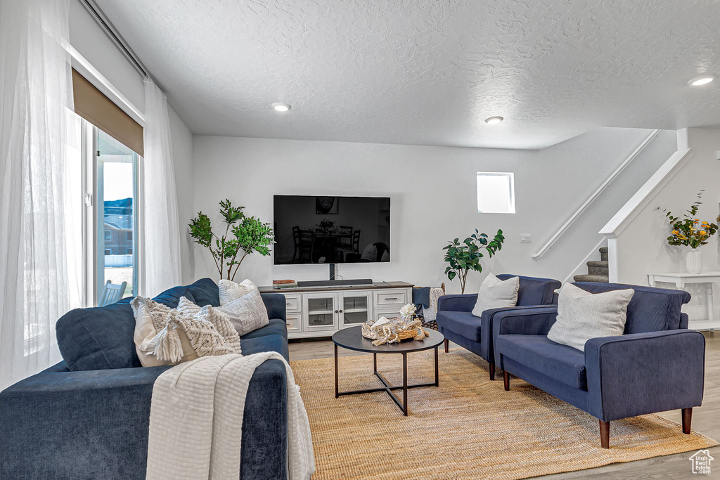 Living room featuring light wood-style floors, a textured ceiling, stairs, and recessed lighting