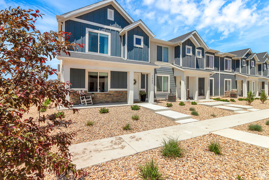 View of front facade featuring board and batten siding, a porch, stone siding, a residential view, and central AC unit