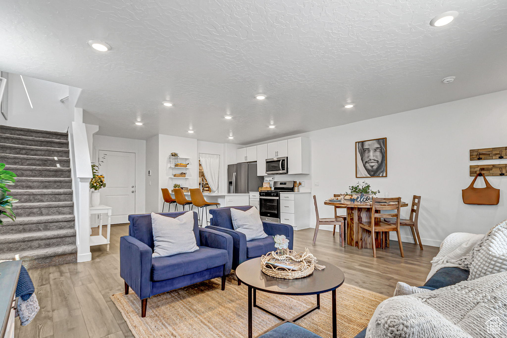 Living room featuring stairs, light wood-style floors, recessed lighting, a textured ceiling, and baseboards