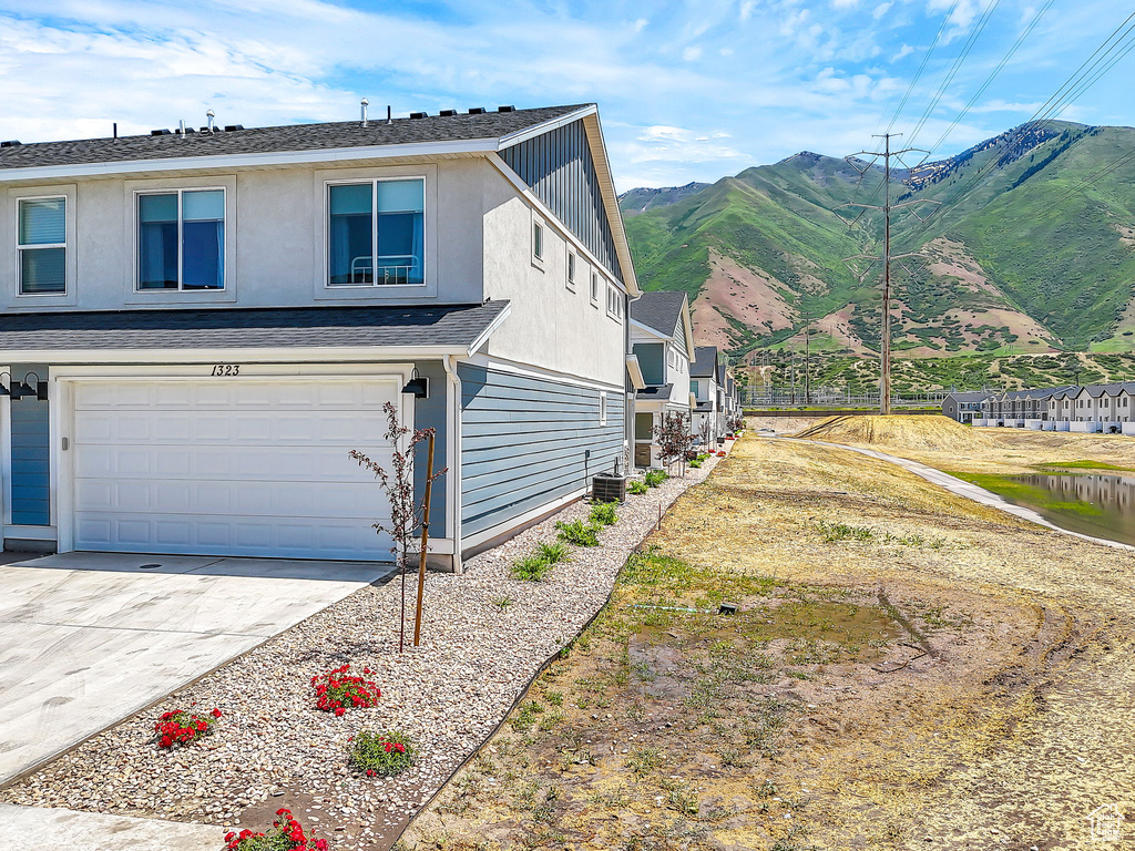 View of property exterior featuring a mountain view, an attached garage, concrete driveway, central AC, and stucco siding