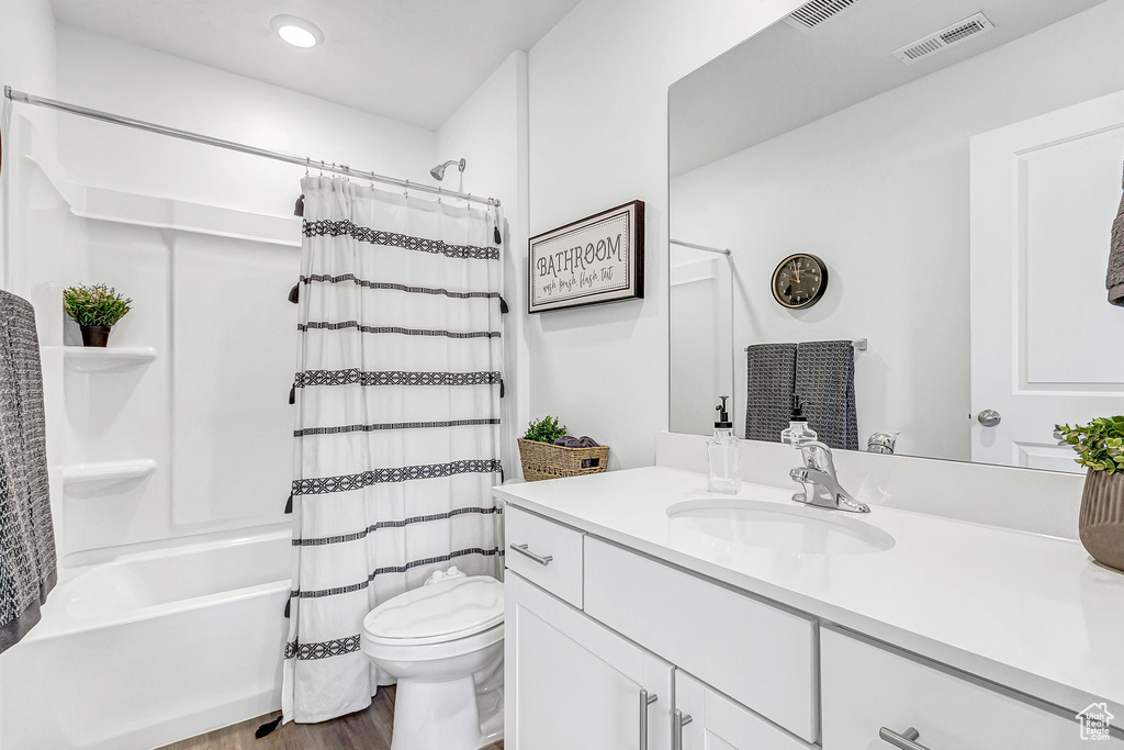 Bathroom featuring vanity, toilet, shower / bathtub combination with curtain, wood finished floors, and recessed lighting
