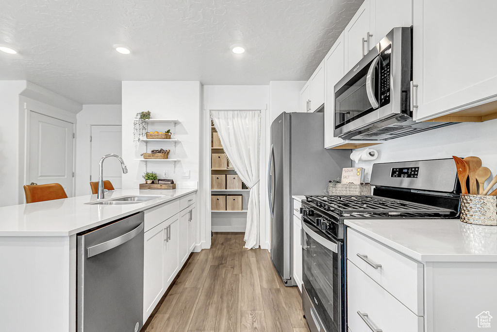 Kitchen featuring stainless steel appliances, a sink, open shelves, a peninsula, and white cabinets