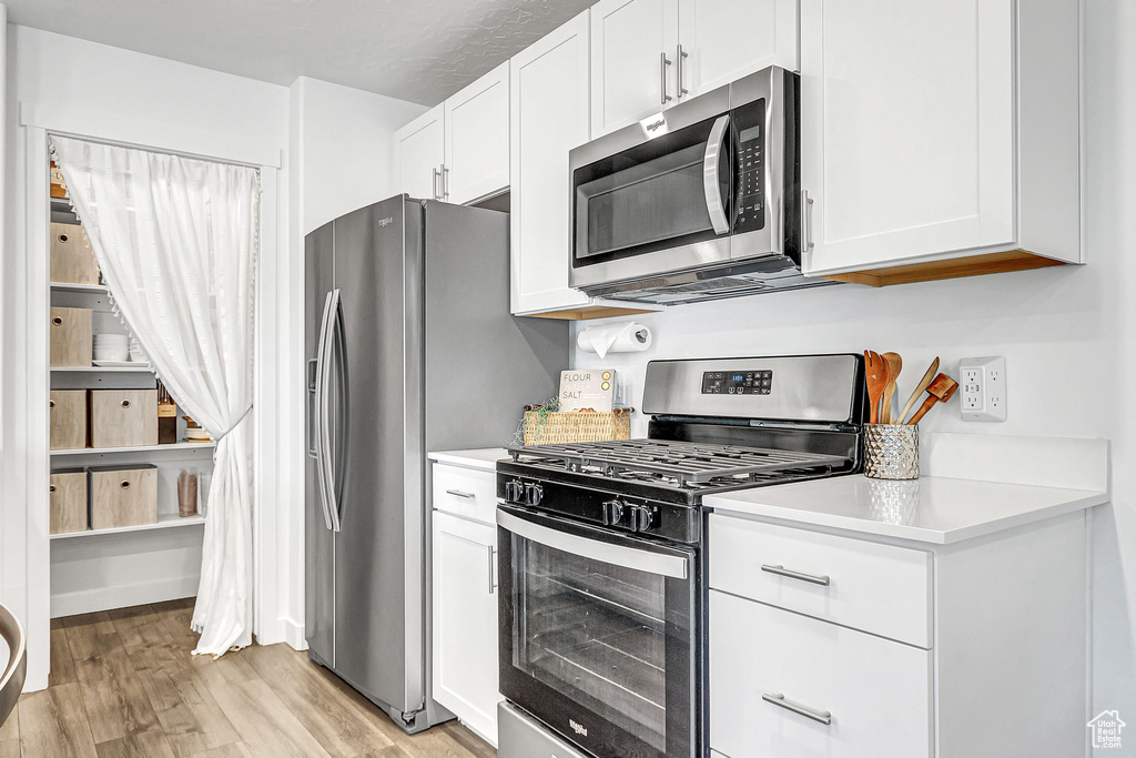 Kitchen featuring stainless steel appliances, light wood-style floors, light countertops, and white cabinets
