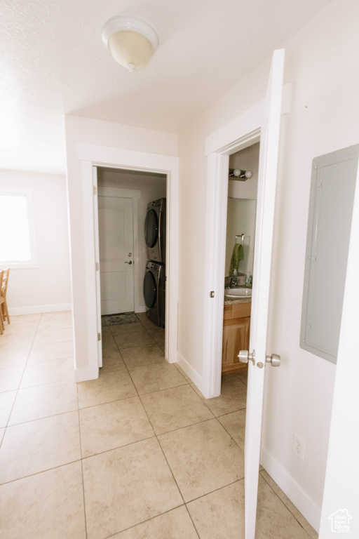Hall featuring stacked washing machine and dryer, light tile patterned floors, electric panel, and baseboards