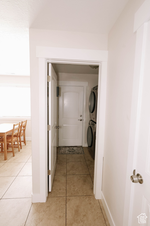 Washroom with stacked washer and clothes dryer, light tile patterned floors, and baseboards