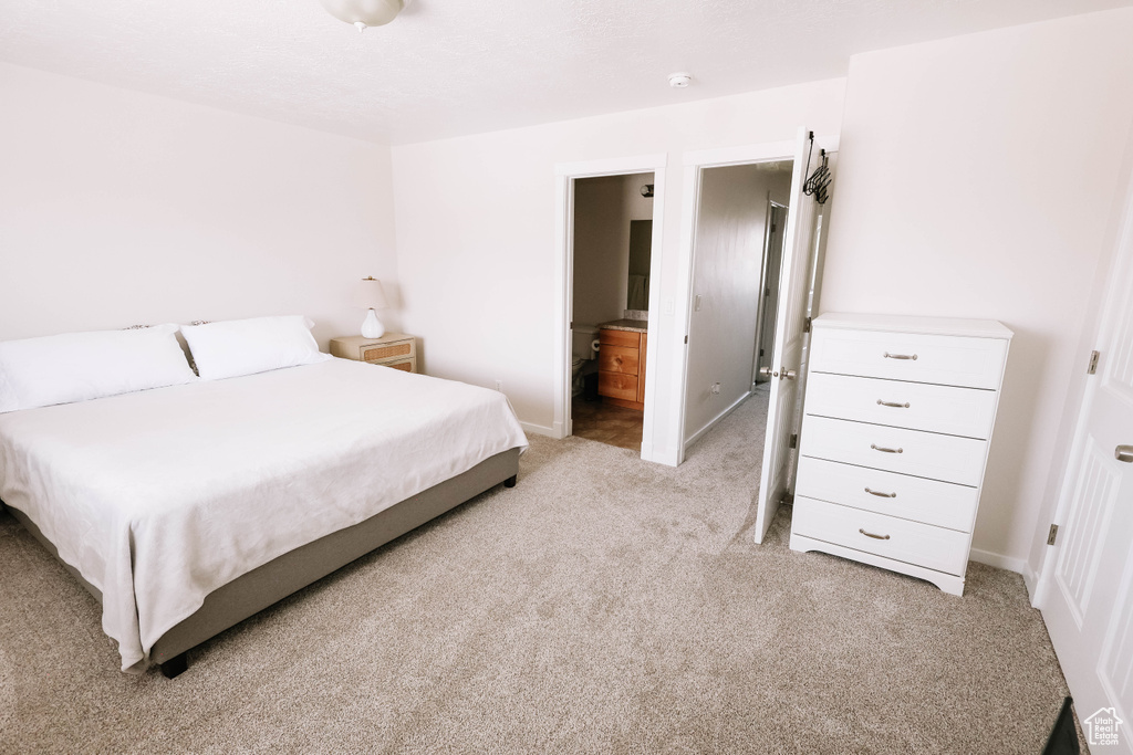 Bedroom with light colored carpet, baseboards, and connected bathroom