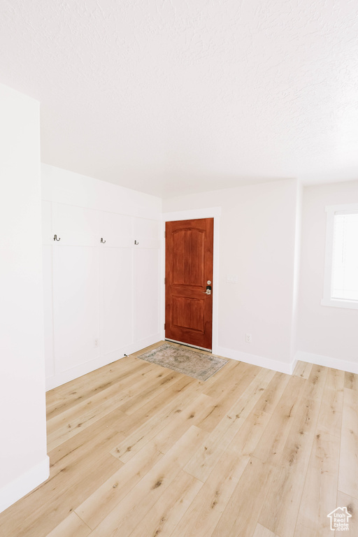 Empty room featuring light wood-style flooring, a textured ceiling, and baseboards