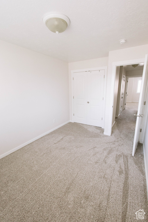 Unfurnished bedroom with baseboards, light colored carpet, and a closet