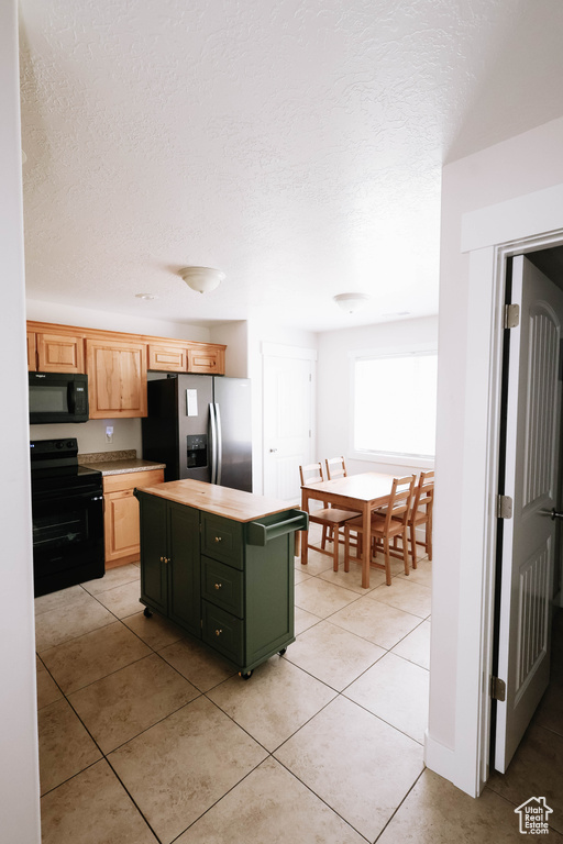 Kitchen with black appliances, a center island, light tile patterned floors, a textured ceiling, and light countertops