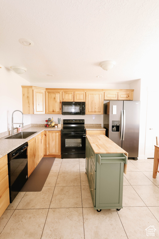 Kitchen featuring black appliances, light brown cabinetry, a sink, green cabinets, and light tile patterned floors