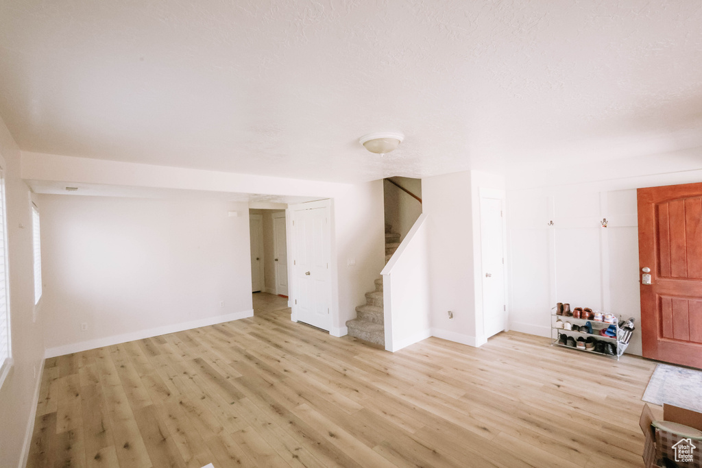 Unfurnished living room featuring stairway, light wood-type flooring, and baseboards