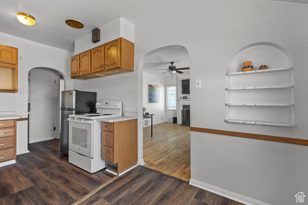 Kitchen featuring white range with electric stovetop, arched walkways, a ceiling fan, a fireplace, and dark wood-type flooring