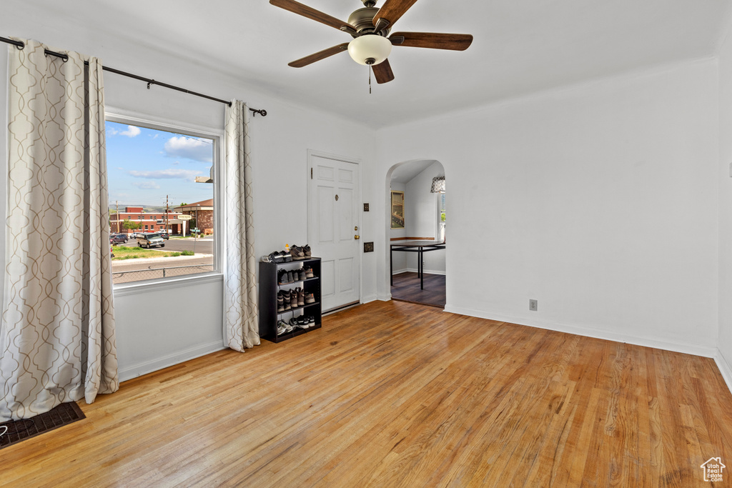 Empty room with arched walkways, ceiling fan, light wood-style floors, and baseboards