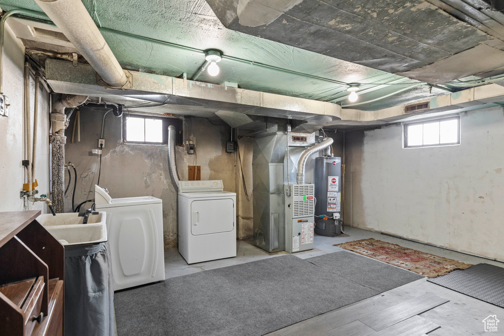 Below grade area featuring washing machine and clothes dryer, heating unit, water heater, and healthy amount of natural light