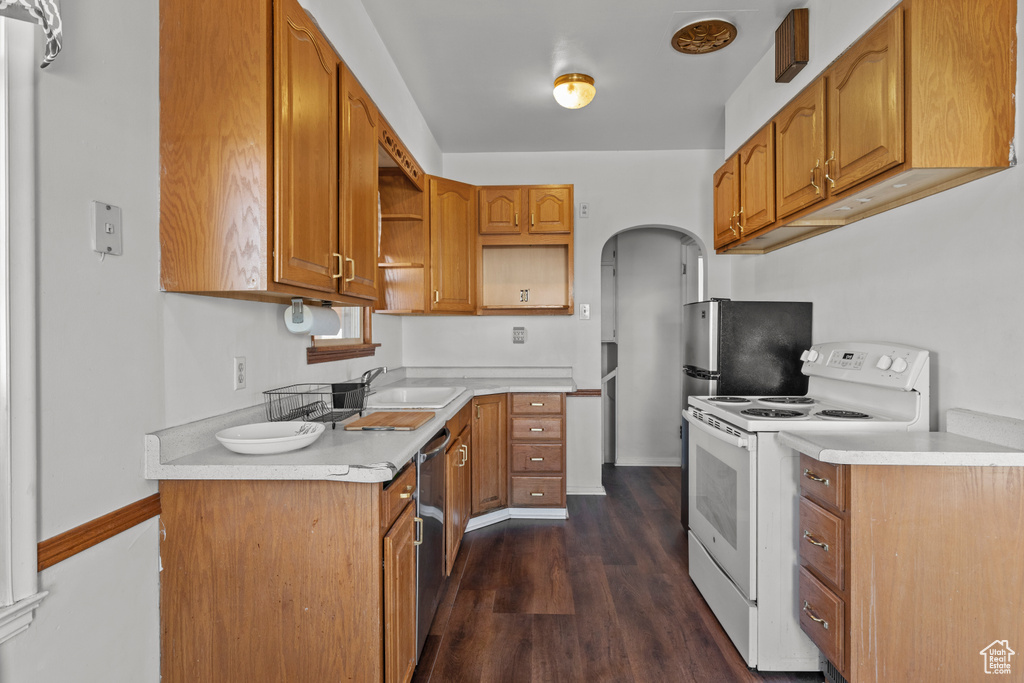 Kitchen with white electric stove, a sink, light countertops, dark wood-style floors, and brown cabinets