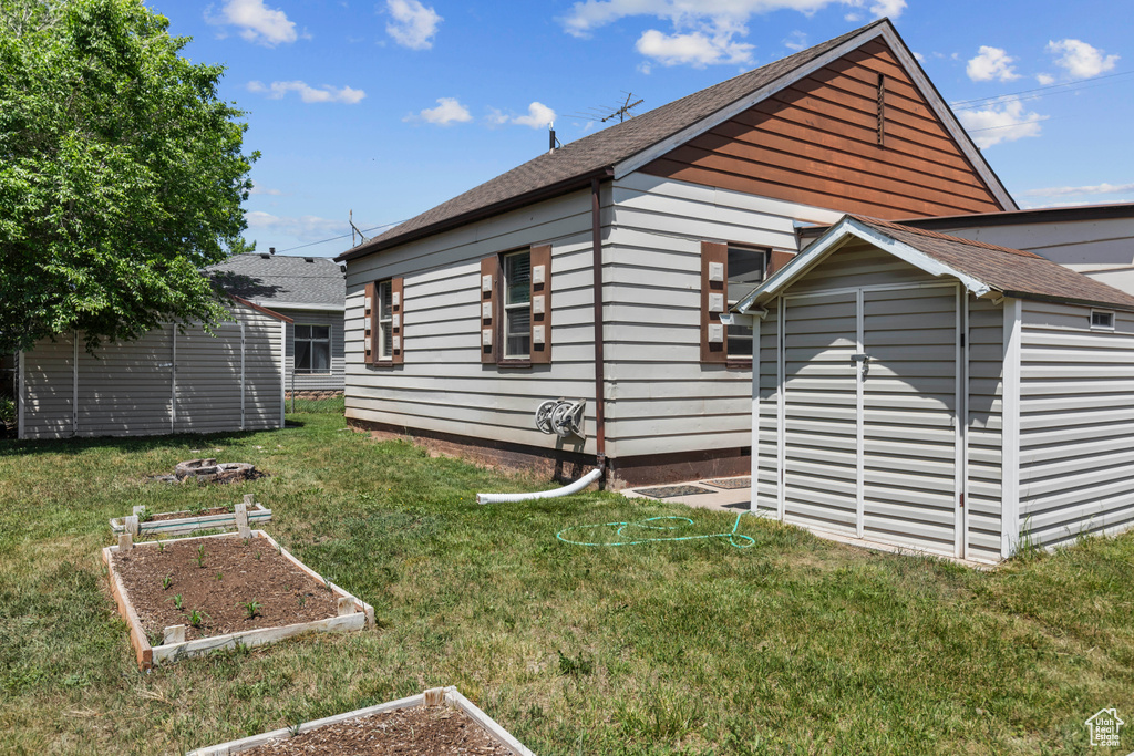 View of side of home with a vegetable garden, a lawn, and roof with shingles