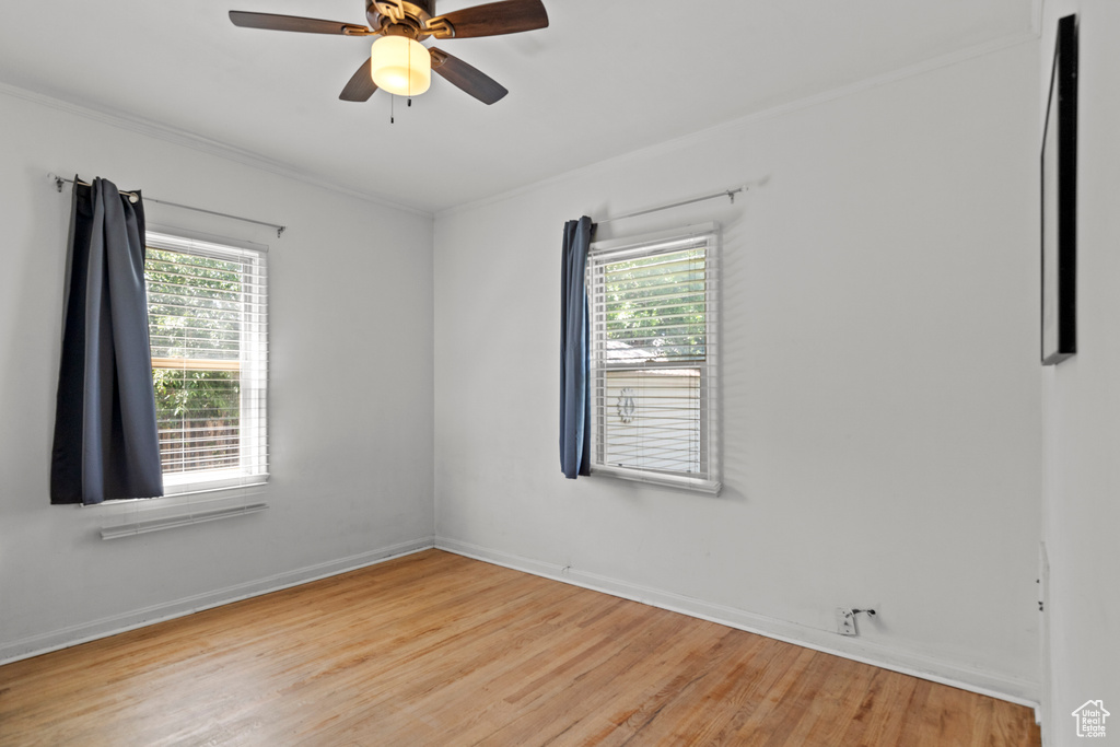 Unfurnished room featuring healthy amount of natural light, light wood-type flooring, ceiling fan, ornamental molding, and baseboards