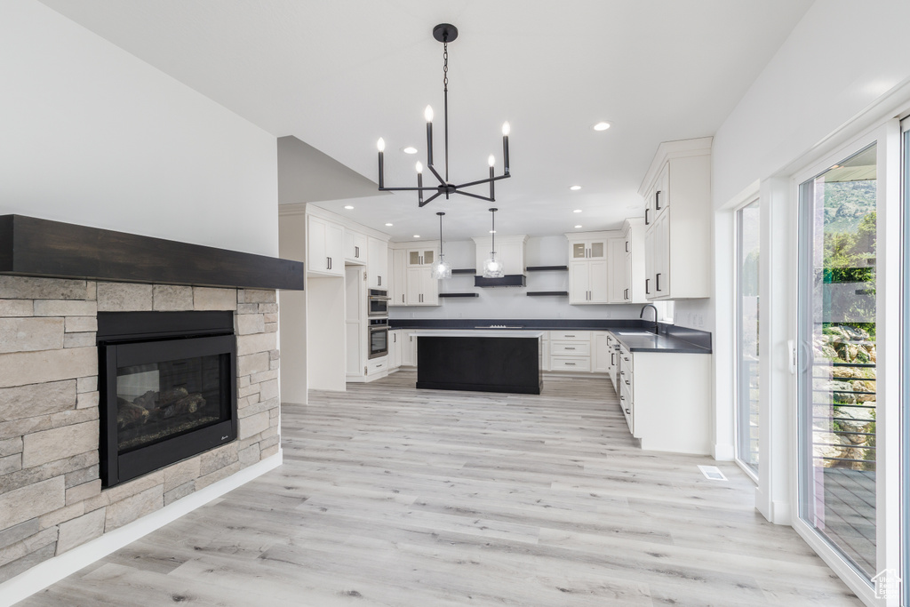 Kitchen with dark countertops, a sink, light wood-type flooring, a kitchen island, and a chandelier