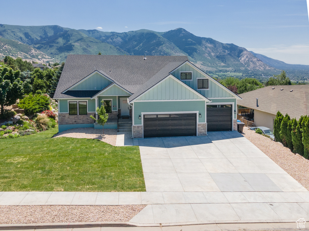 Craftsman house with board and batten siding, a garage, stone siding, driveway, and a front yard