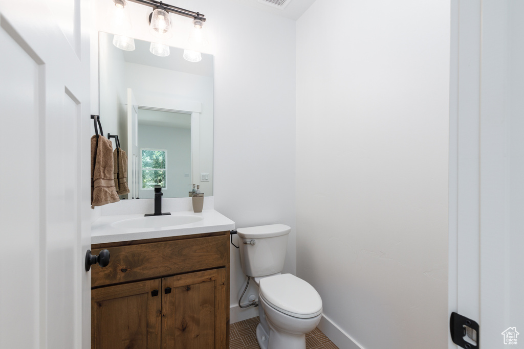 Half bathroom with vanity, toilet, baseboards, and tile patterned floors