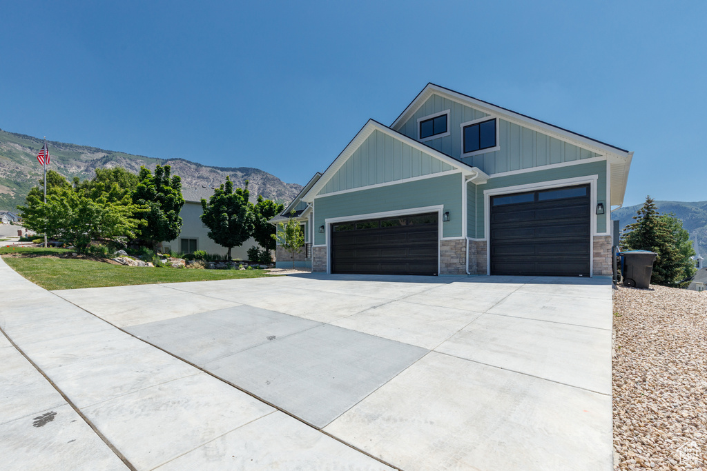 View of front of property featuring driveway, a mountain view, a garage, stone siding, and board and batten siding