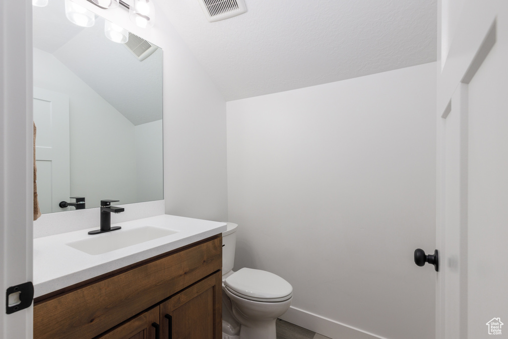 Half bathroom featuring vaulted ceiling, vanity, toilet, and baseboards