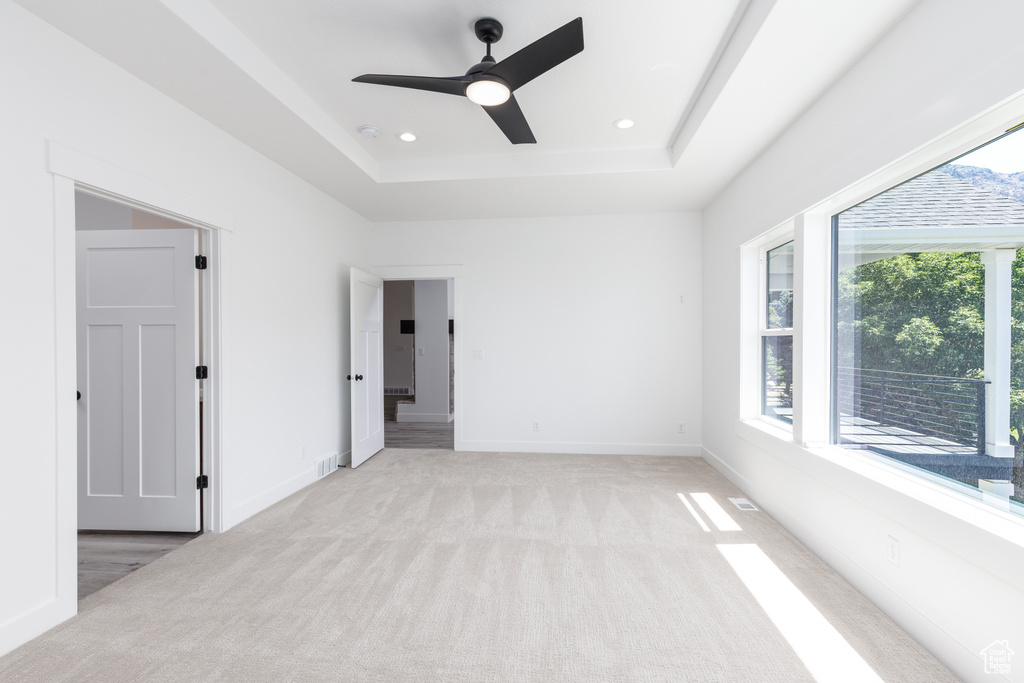 Unfurnished bedroom featuring light carpet, a tray ceiling, recessed lighting, baseboards, and ceiling fan