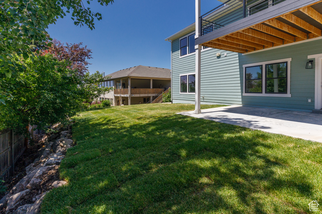 View of grassy yard featuring a patio and a balcony