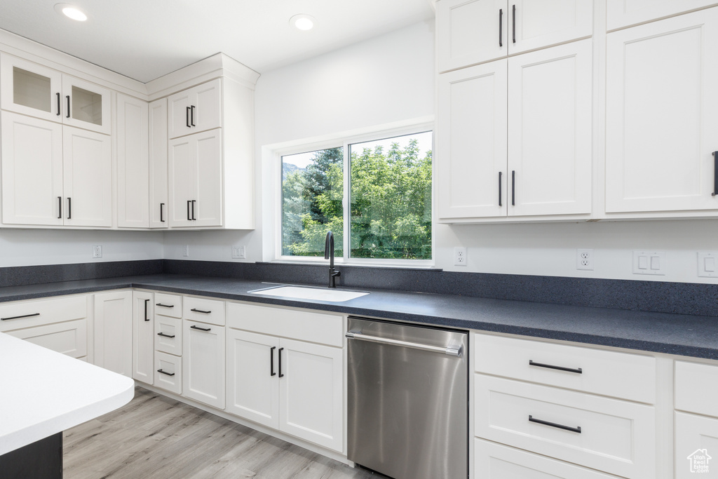 Kitchen featuring dishwasher, a sink, white cabinetry, dark countertops, and recessed lighting