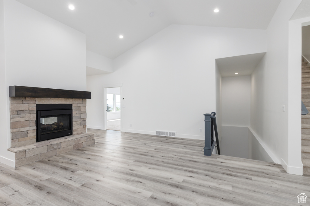 Unfurnished living room with high vaulted ceiling, stairway, wood finished floors, a fireplace, and recessed lighting