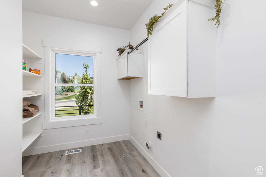 Washroom with cabinet space, electric dryer hookup, washer hookup, light wood-style flooring, and baseboards
