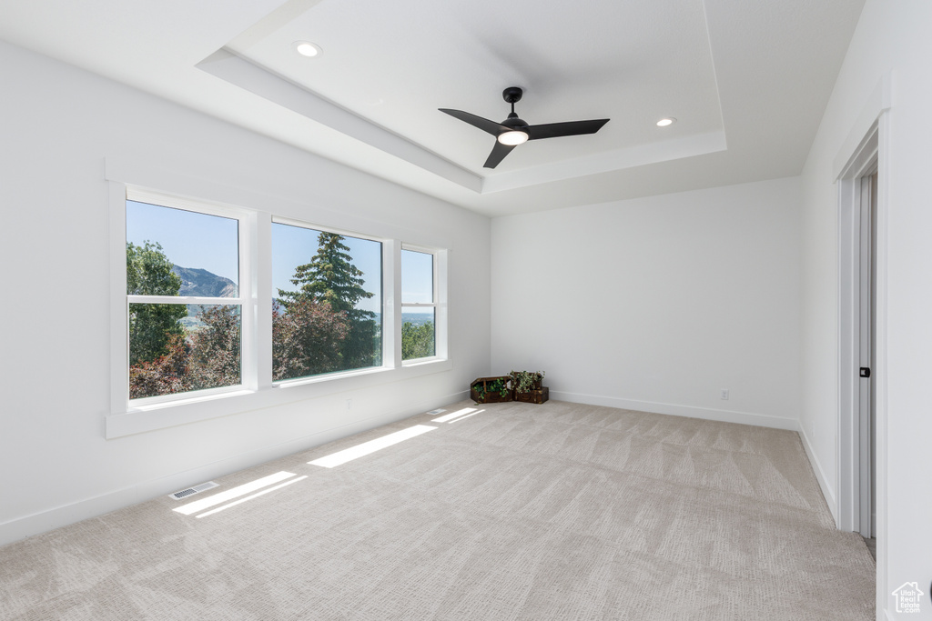 Empty room featuring a raised ceiling, light carpet, recessed lighting, a ceiling fan, and baseboards