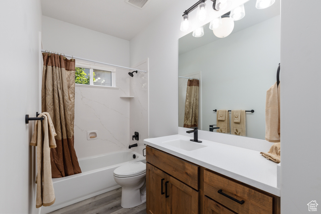 Full bath with vanity, shower / bath combination with curtain, wood finished floors, and toilet