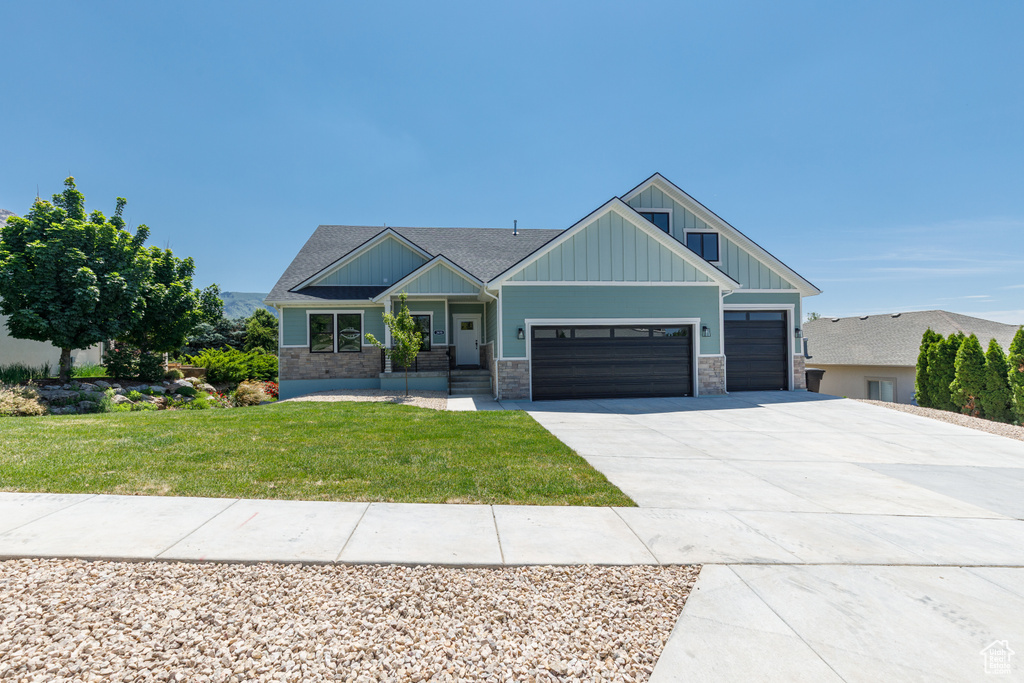 Craftsman-style home with board and batten siding, a garage, driveway, a front lawn, and stone siding