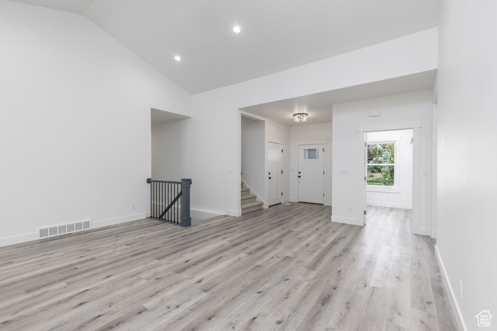 Unfurnished room featuring light wood finished floors, baseboards, stairs, recessed lighting, and high vaulted ceiling