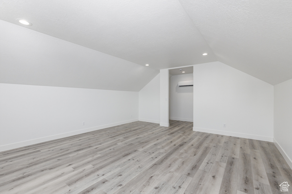 Additional living space with vaulted ceiling, recessed lighting, a wall mounted air conditioner, light wood-style flooring, and baseboards