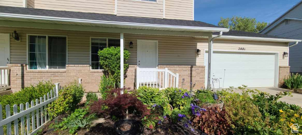 Doorway to property featuring brick siding, a porch, and an attached garage