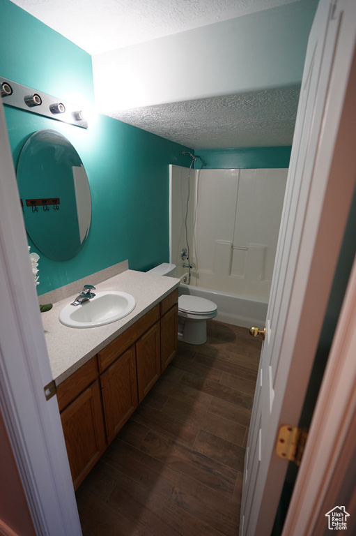 Bathroom with wood finished floors, vanity, a textured ceiling, toilet, and shower / bathtub combination