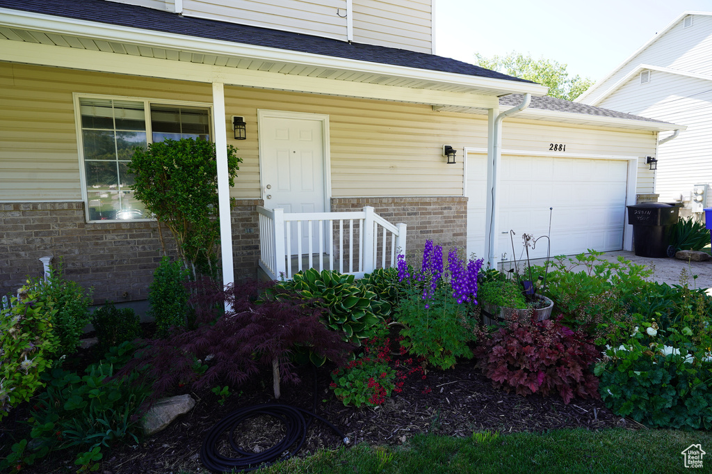 Entrance to property with brick siding, a garage, a shingled roof, and covered porch