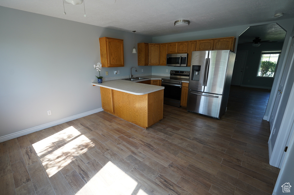 Kitchen with appliances with stainless steel finishes, a sink, a peninsula, a ceiling fan, and light countertops