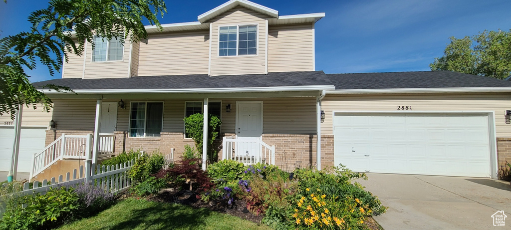 View of front facade featuring covered porch, brick siding, driveway, and a garage