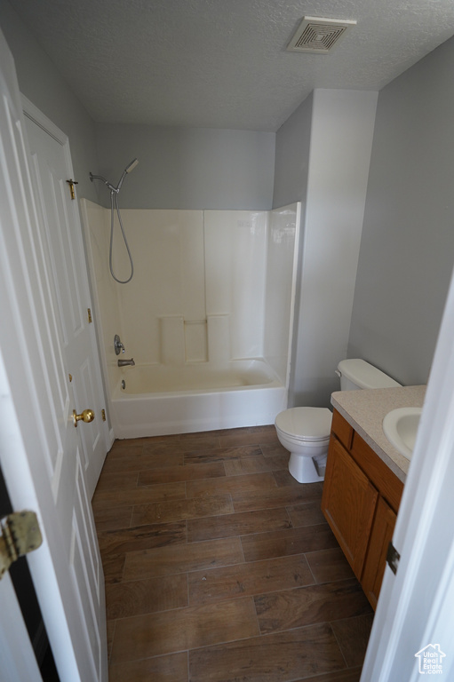 Bathroom with vanity, wood finished floors, toilet, shower / washtub combination, and a textured ceiling
