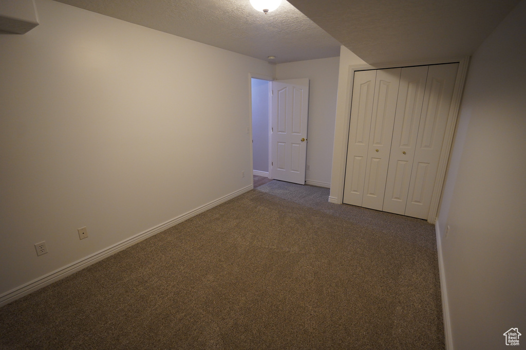 Unfurnished bedroom with carpet flooring, a textured ceiling, baseboards, and a closet