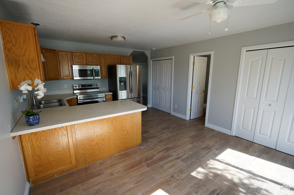 Kitchen featuring appliances with stainless steel finishes, light countertops, a peninsula, and wood finished floors