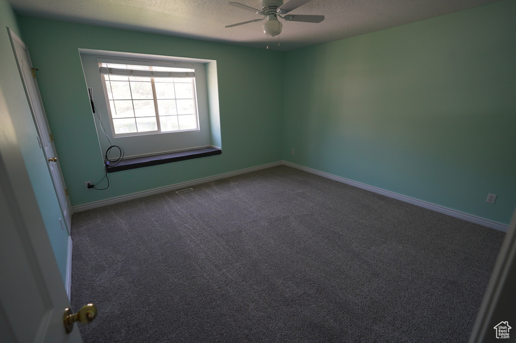 Empty room featuring a textured ceiling, a ceiling fan, dark colored carpet, and baseboards