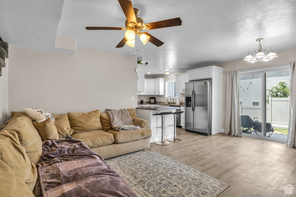 Living area featuring a chandelier, light wood-type flooring, a ceiling fan, and a textured ceiling