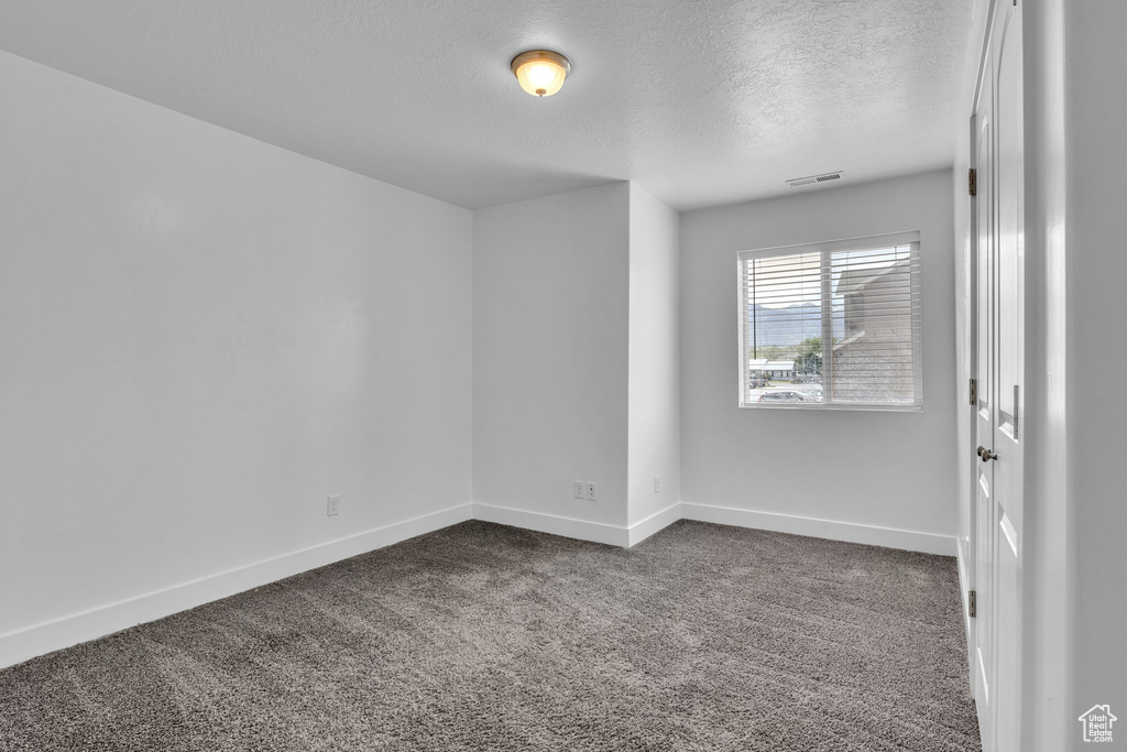 Spare room with a textured ceiling, baseboards, and dark colored carpet