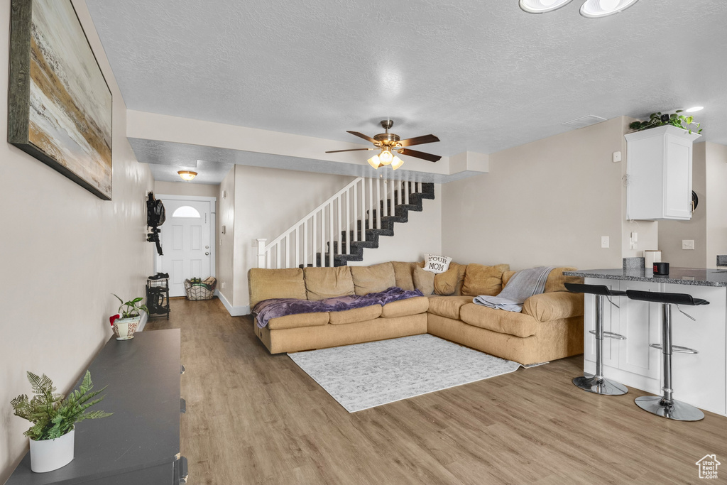 Living area with light wood-type flooring, stairway, a textured ceiling, a ceiling fan, and baseboards